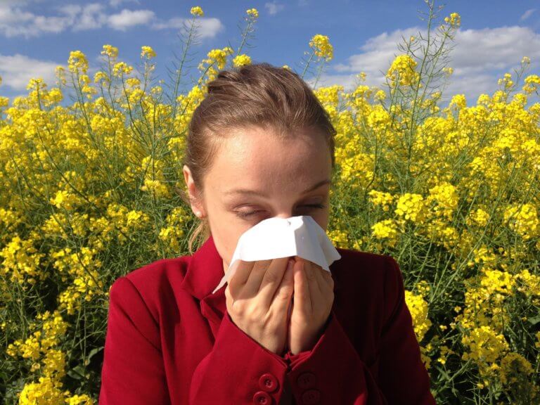 girl with allergies in a yellow flower field blowing her nose